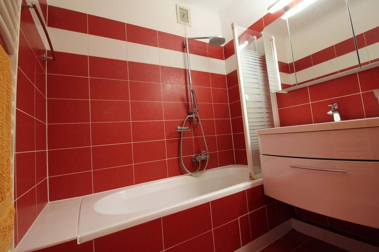 Badezimmer mit roten und weißen Fliesen, Badewanne mit Duschfunktion und Waschtisch.