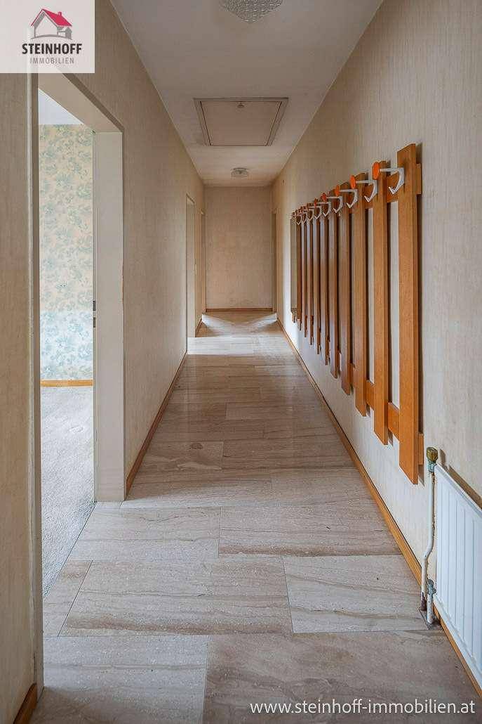 Langer Flur mit hellen Fliesen, Holzgarderobe und Zugang zu weiteren Räumen.