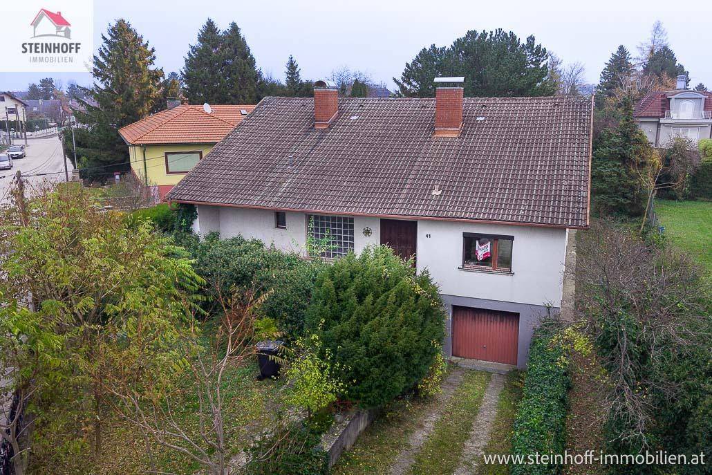 Einfamilienhaus mit Satteldach, Garage und umgebendem Gartenbereich.