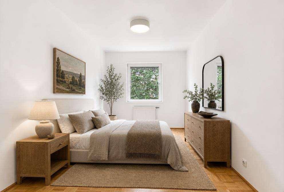 Helles Schlafzimmer mit beigem Teppich, Holzboden und einem großen Fenster mit Blick ins Grüne.