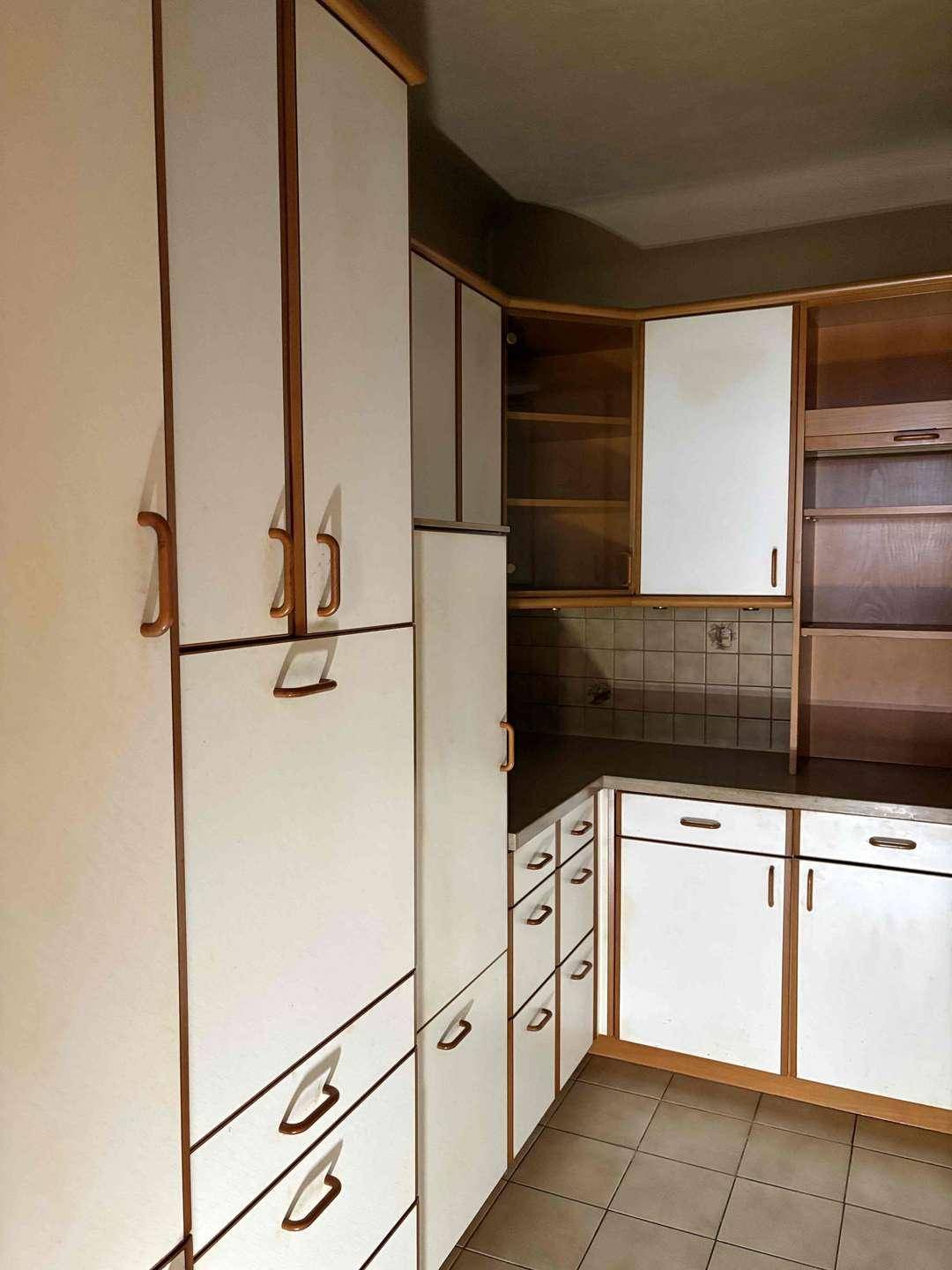 Küche mit hohen weißen und holzfarbenen Schränken, Fliesenboden und viel Stauraum.