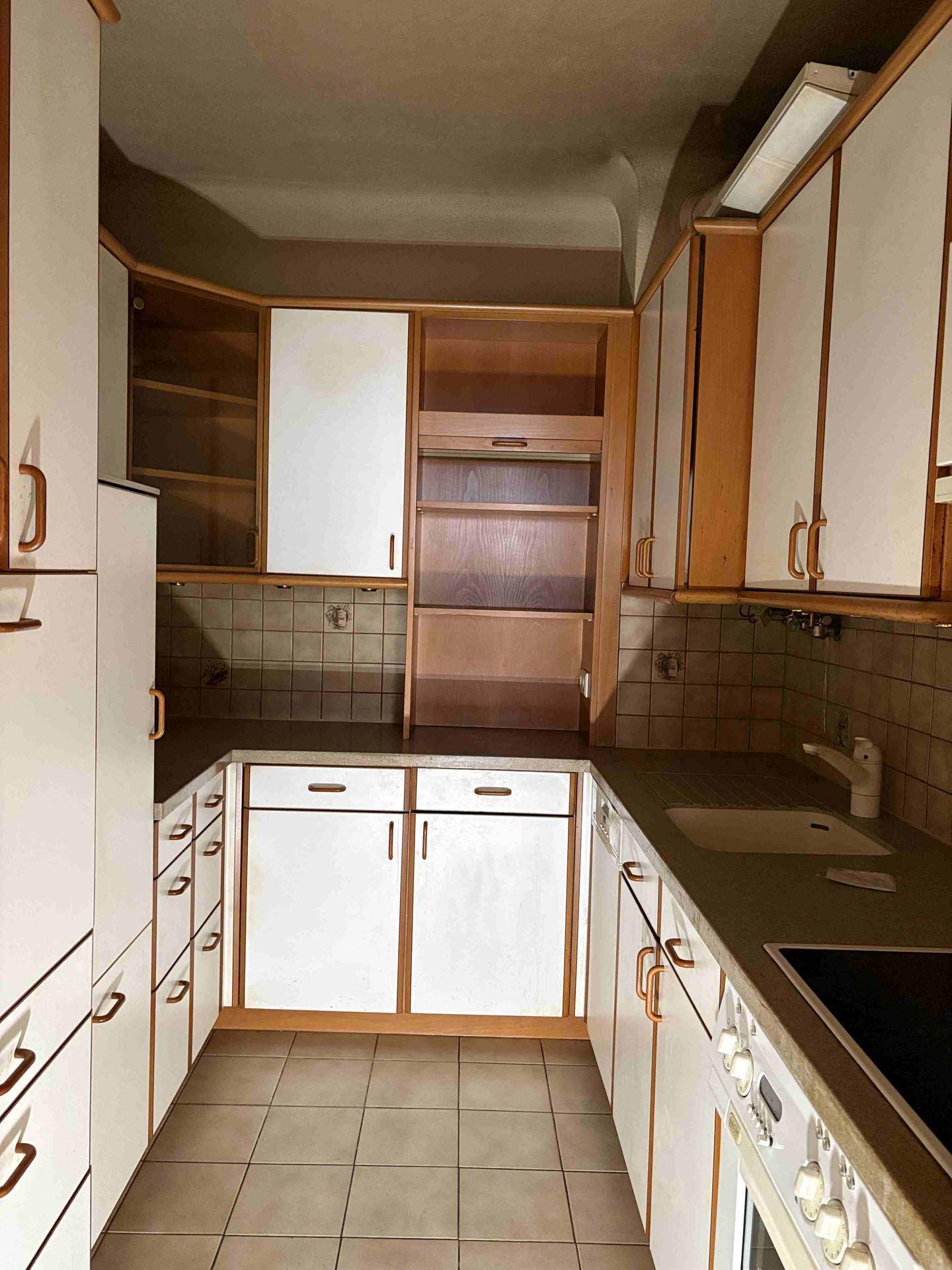 Ältere Einbauküche mit weißen Schränken, Fliesenboden und integrierten Geräten, bereit zur Modernisierung.