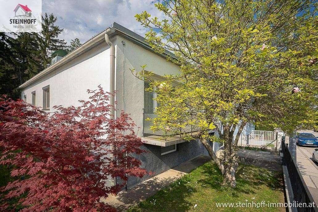 Seitenansicht des Hauses mit kleinem Balkon und üppiger Vegetation im Vorgarten.