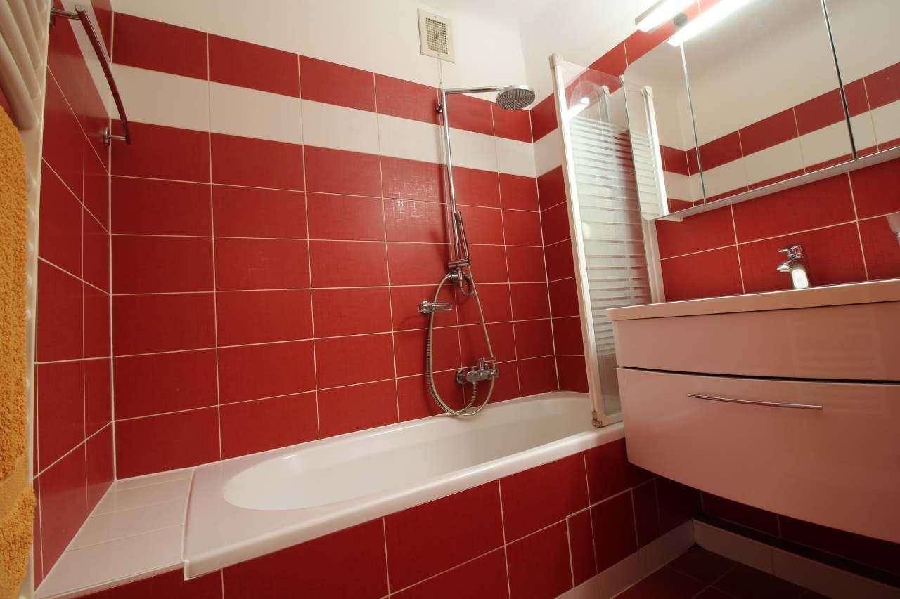 Badezimmer mit auffälligen rot-weißen Fliesen, Badewanne mit Duschfunktion und Waschtisch.