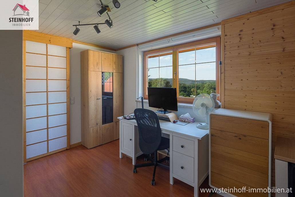 Helles Arbeitszimmer mit Schreibtisch, Holzmöbeln und Blick ins Grüne.