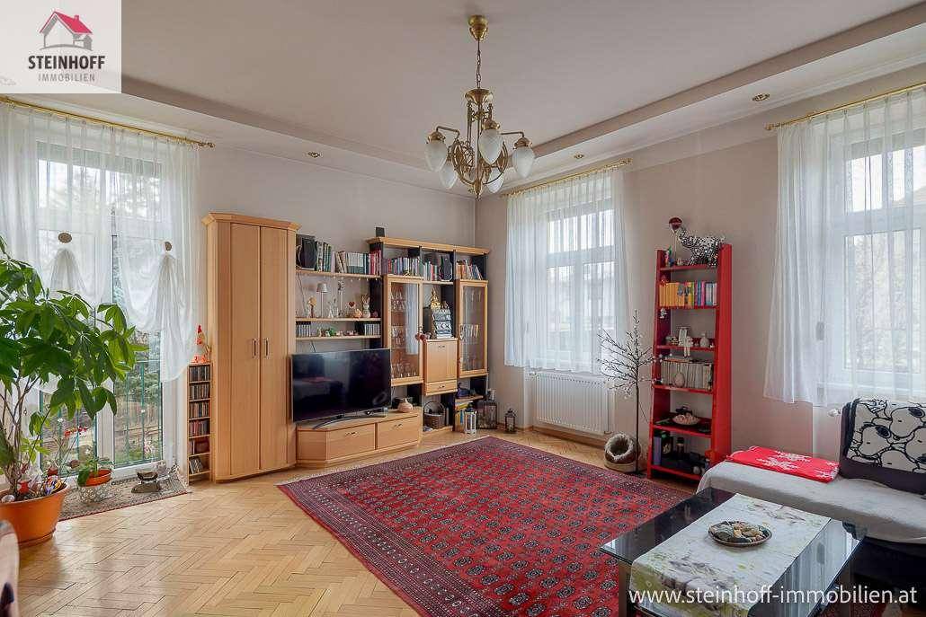 Geräumiges Wohnzimmer mit Fischgrätparkett, großen Fenstern und traditioneller Möblierung.