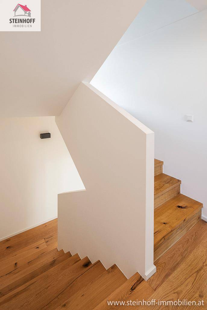 Moderne Holztreppe mit weißem Geländer und Wänden, die die verschiedenen Stockwerke stilvoll verbindet.