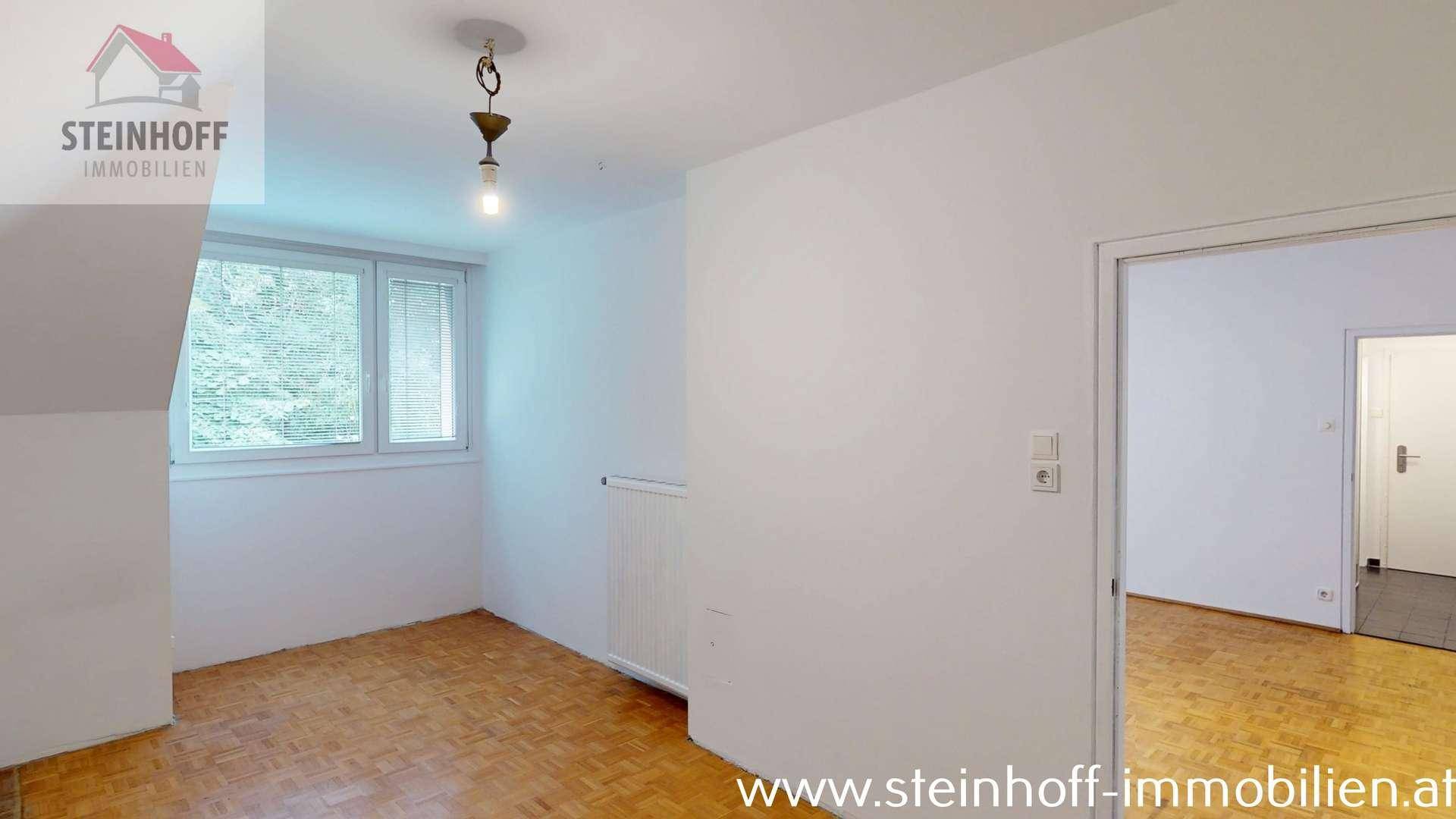 Heller Raum mit Parkettboden, Fenster, Dachschrägen und Zugang zu einem weiteren Zimmer.