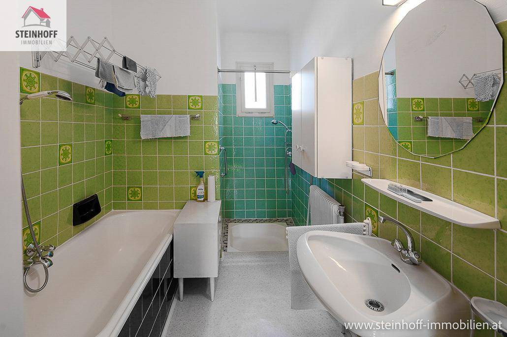 Badezimmer mit grünen Fliesen, Badewanne, Dusche und Waschbecken.