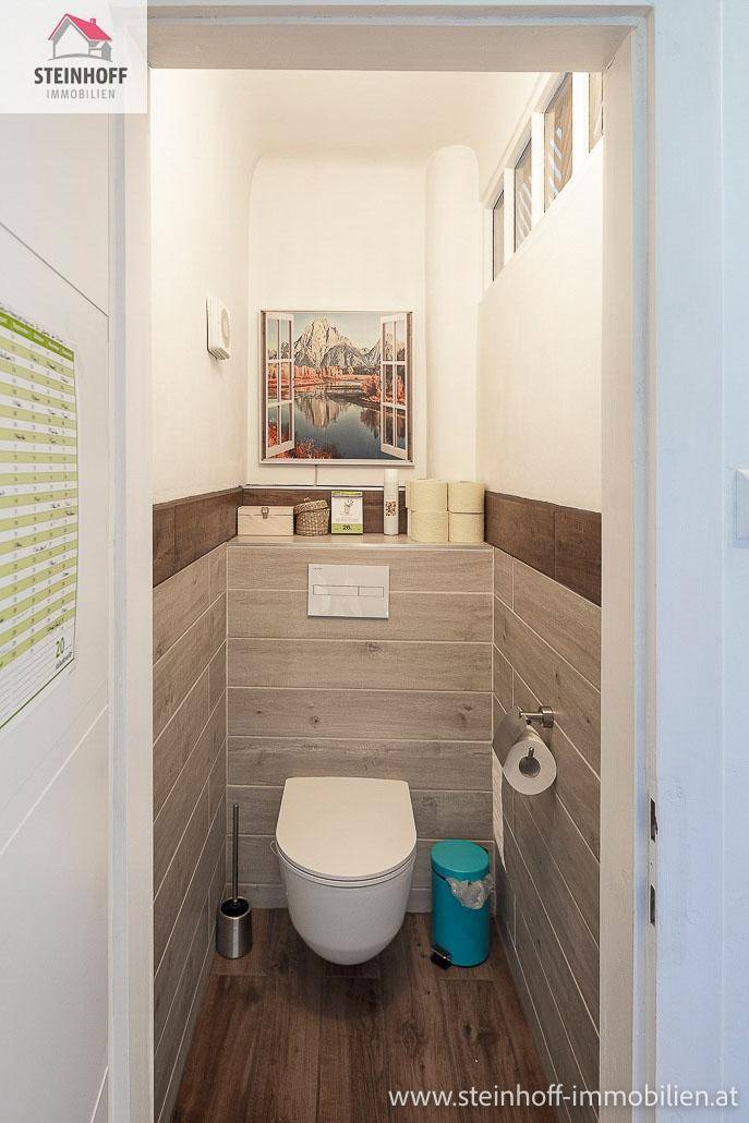 Modernes Gäste-WC mit Wand-WC, Holzoptikfliesen und dekorativem Bild.