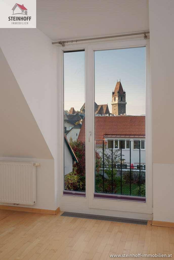 Heller Raum mit Holzboden, Dachschräge und Blick auf einen Kirchturm in der Ferne.