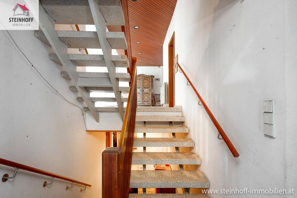 Treppenhaus mit Steinstufen und Holzgeländer, das die verschiedenen Ebenen des Hauses verbindet.