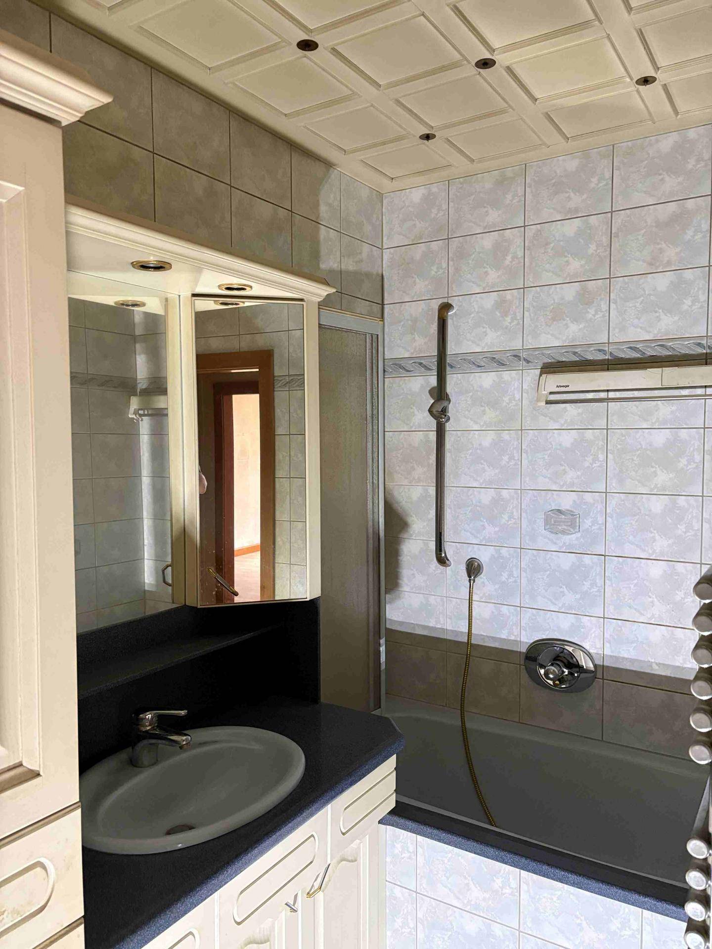 Badezimmer mit Badewanne, Waschbecken und Spiegelschrank, gefliest in hellen Tönen.