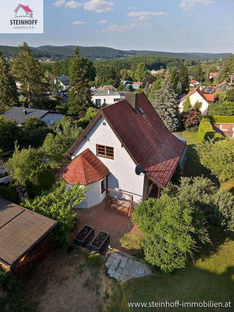 Freistehendes Haus mit rotem Dach und gepflegtem Garten in grüner Umgebung.