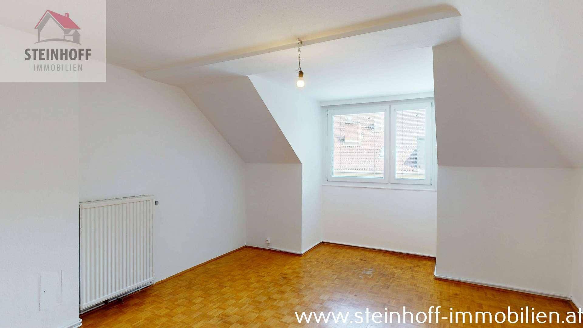Heller Raum mit Parkettboden, Fenster, Heizkörper und Dachschrägen.