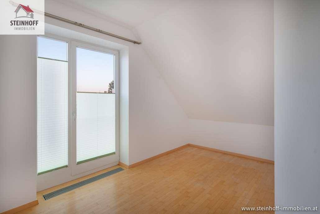Unmöblierter Raum mit Holzboden, Dachschräge und einem Fenster mit Sichtschutz.