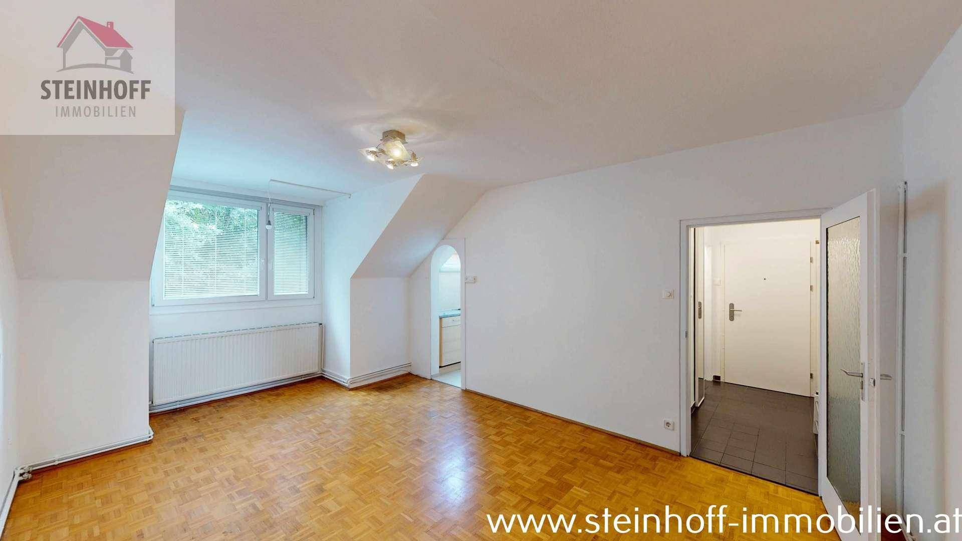 Heller Raum mit Parkettboden, Dachschrägen und Zugang zu einem gefliesten Bereich.