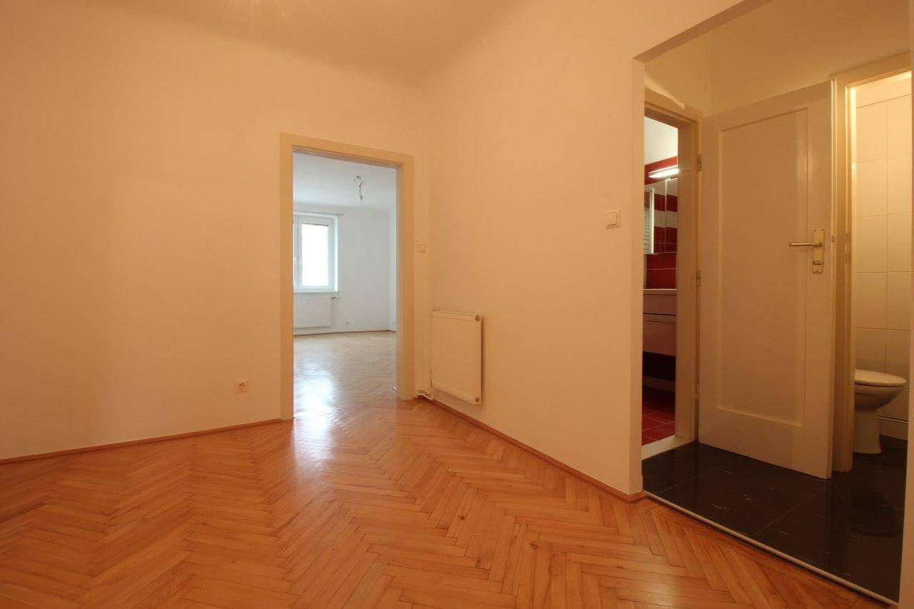 Heller Flur mit Fischgrätparkett, der zu einem Zimmer und einem Badezimmer führt.