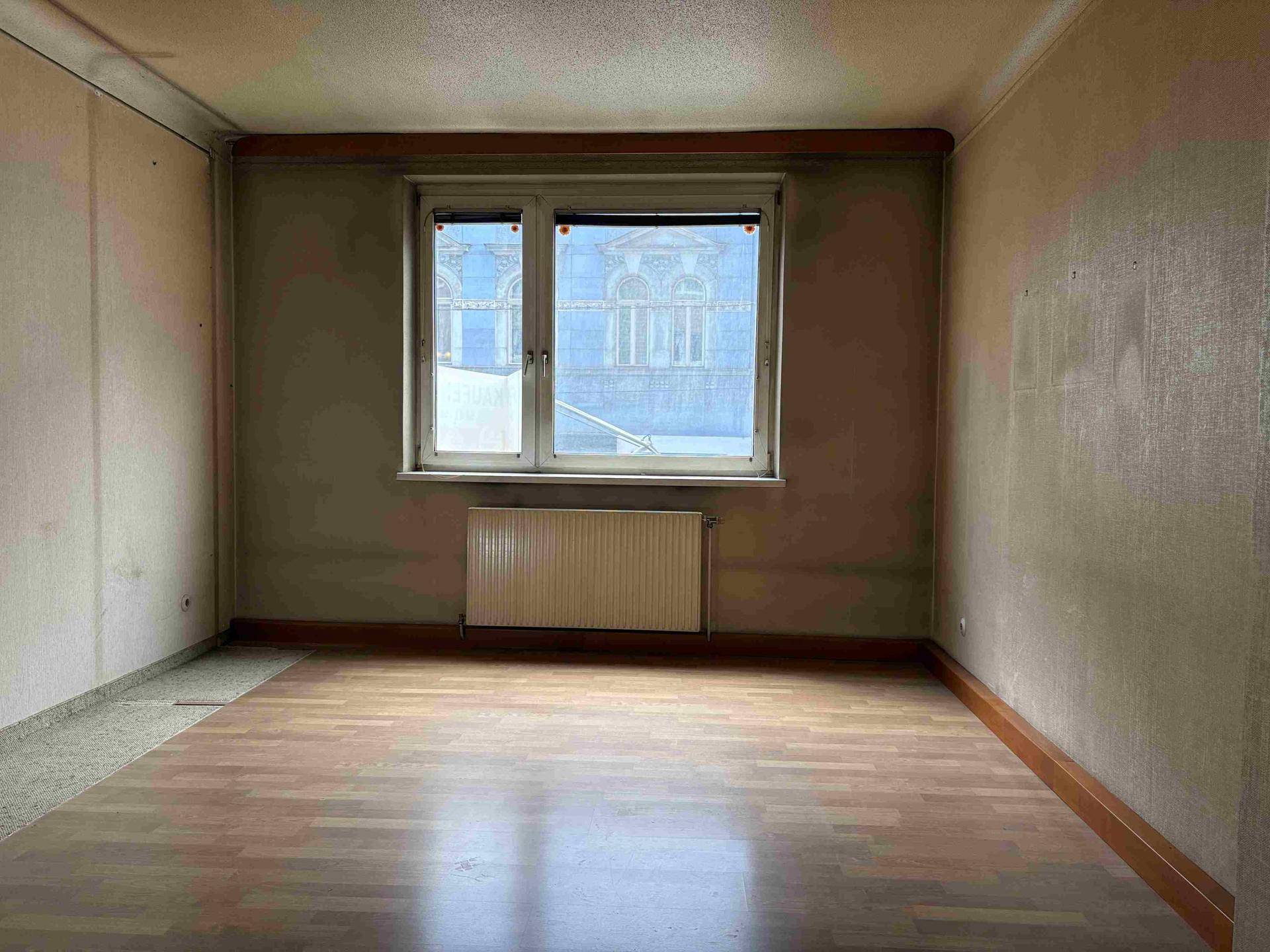 Leeres Zimmer mit Holzparkettboden und Fenster, das auf ein Gebäude blickt, bereit zur Renovierung.