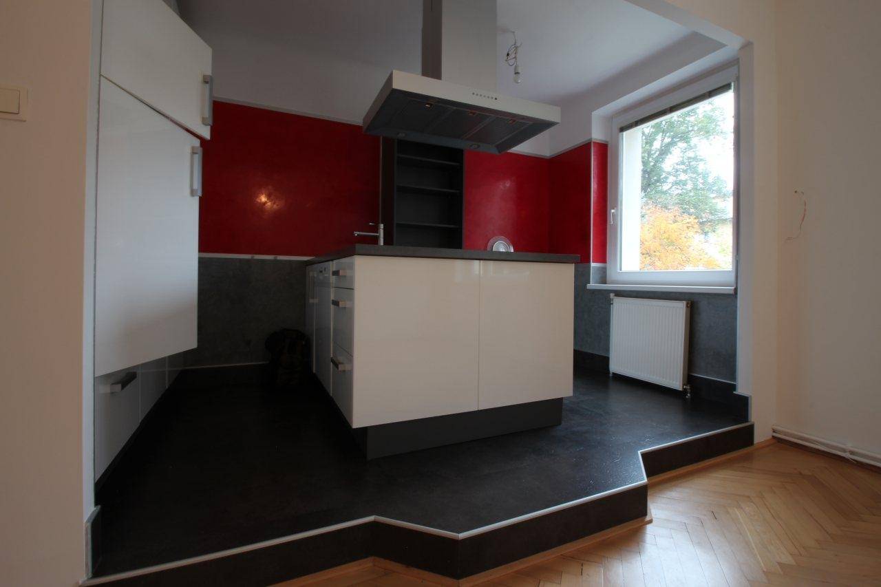 Moderne Küche mit roten Wänden, Kochinsel, Dunstabzugshaube und Blick ins Grüne.