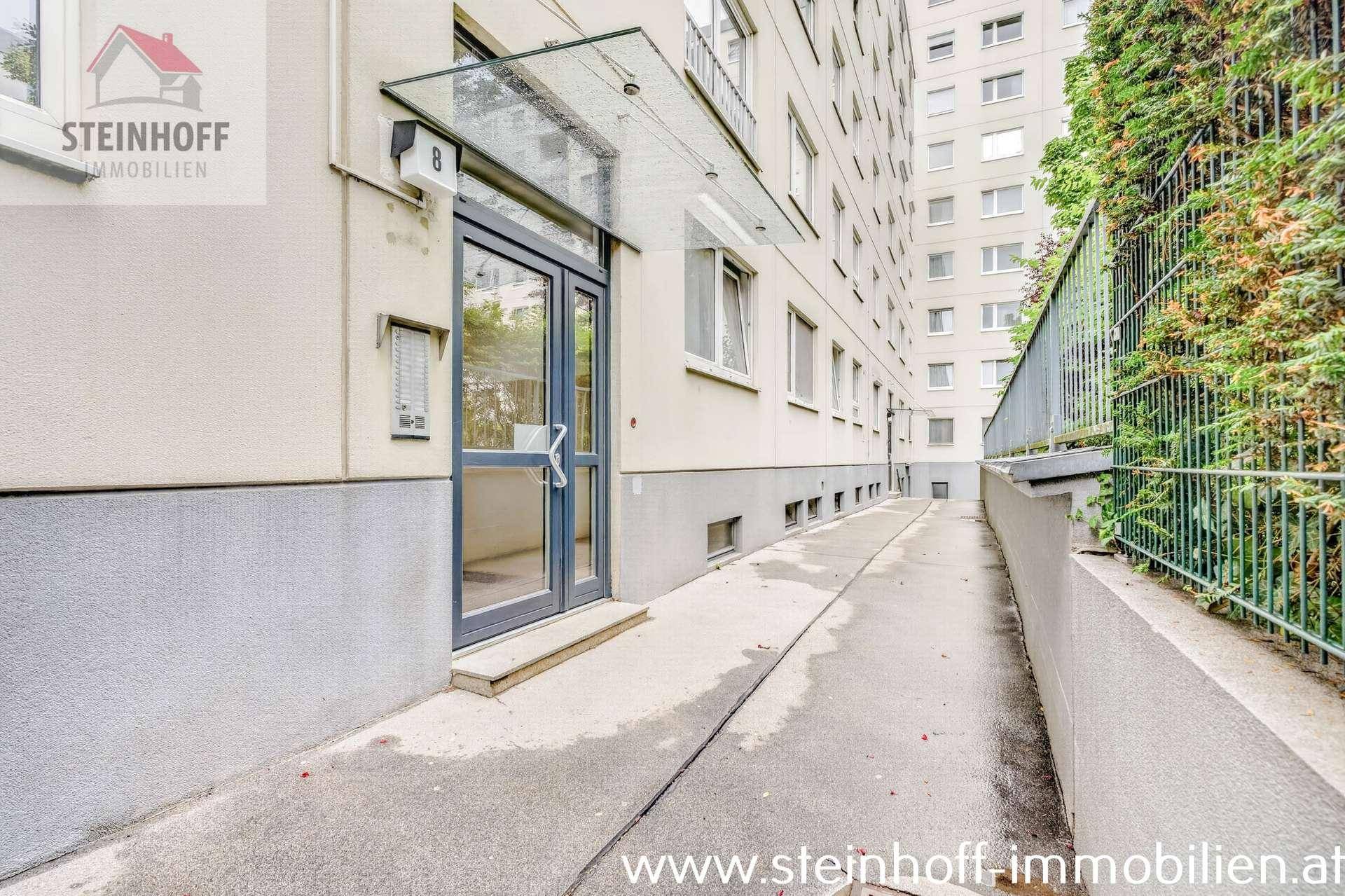 Eingangsbereich eines Mehrfamilienhauses mit Rampe für barrierefreien Zugang und moderner Tür.