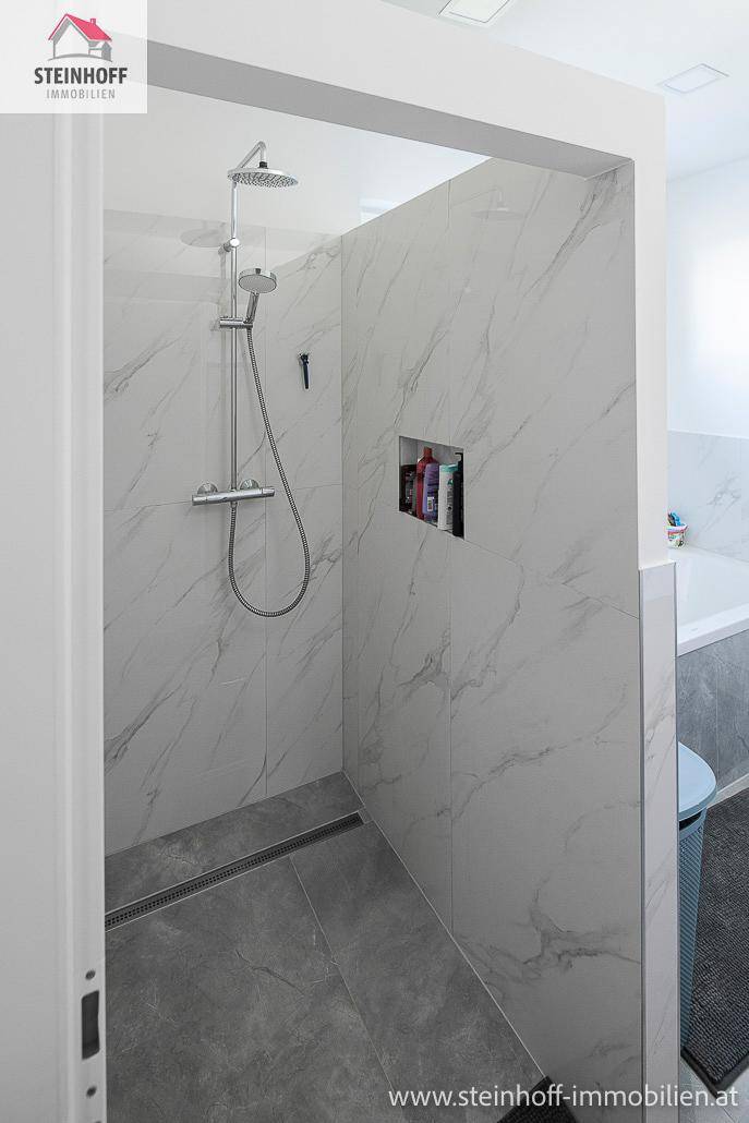Moderne begehbare Dusche mit großformatigen Fliesen in Marmoroptik und einem Regenduschkopf.