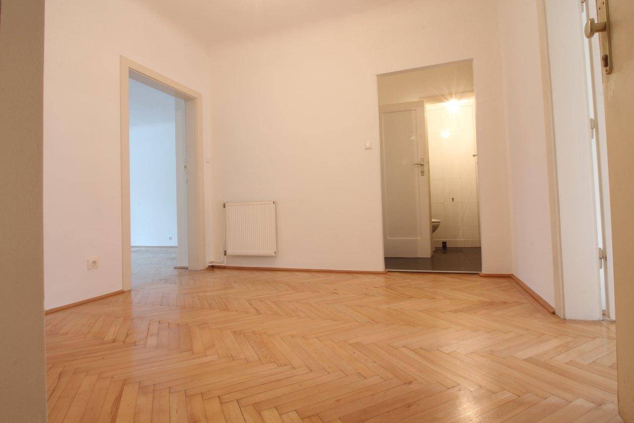 Flur mit Fischgrätparkett, der zu einem weiteren Zimmer und einem Badezimmer führt.
