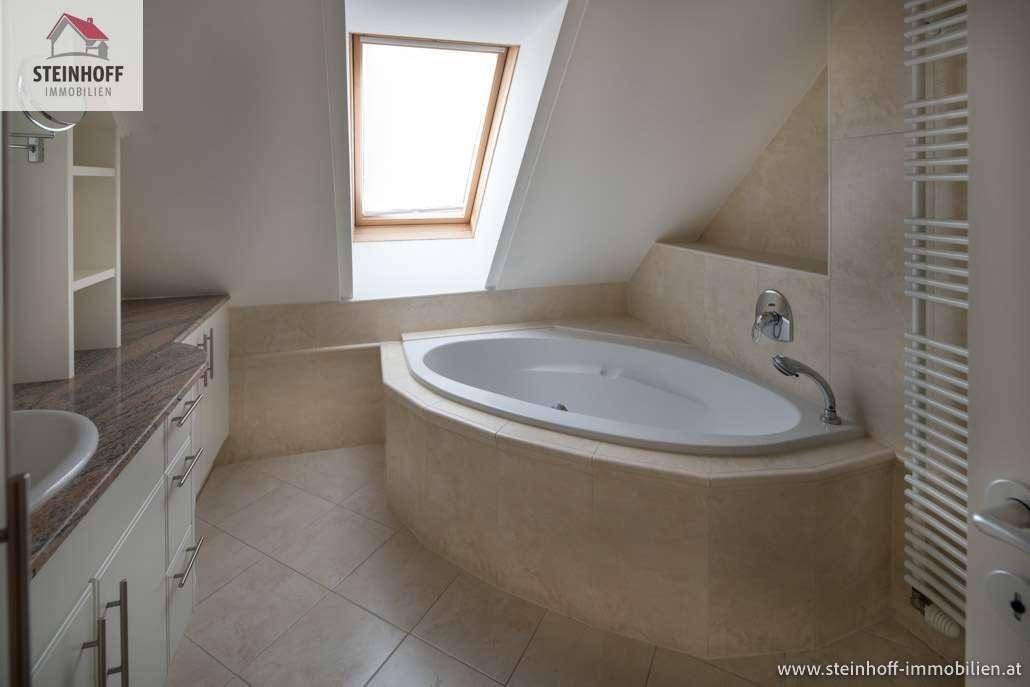 Helles Badezimmer mit Eckbadewanne, Waschtisch, Fliesenboden und einem Dachfenster.