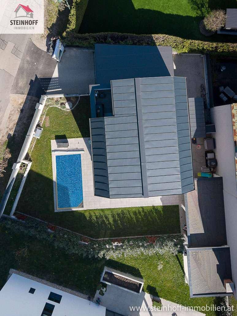 Vogelperspektive des modernen Hauses mit Pool und gepflegtem Gartenbereich unter blauem Himmel.