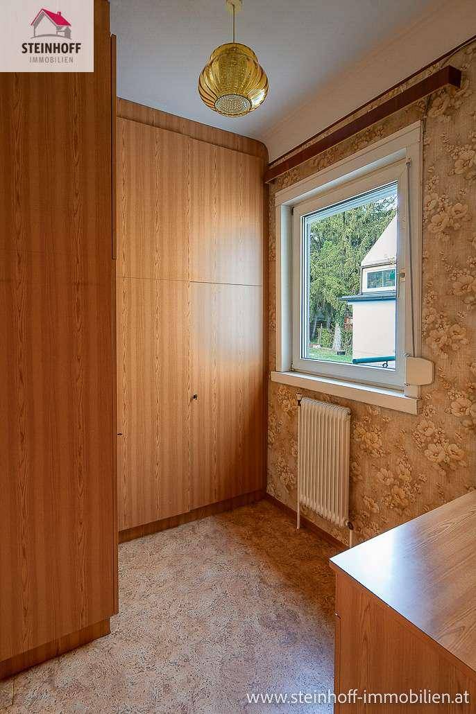 Zimmer mit Einbauschrank aus Holz und Fenster, das viel Tageslicht hereinlässt.
