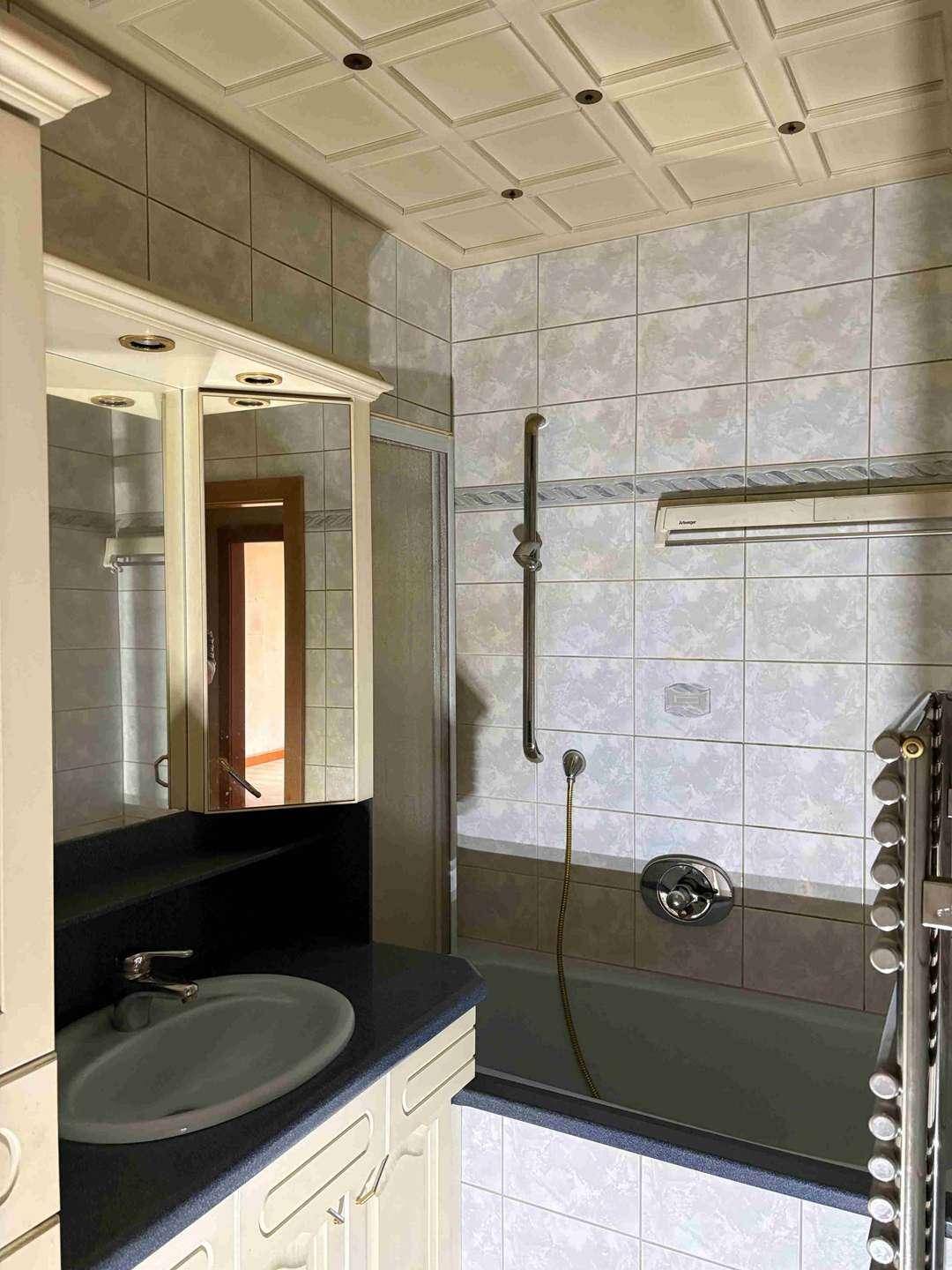 Badezimmer mit Badewanne, Waschtisch, Spiegelschrank und gefliesten Wänden sowie Decke.