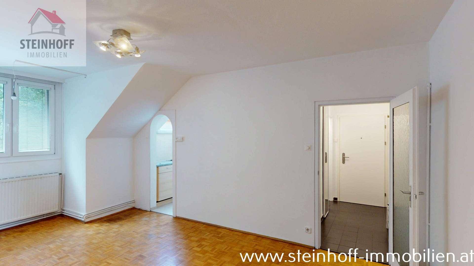 Heller Raum mit Parkettboden, Dachschrägen und Zugang zu einem gefliesten Bereich.