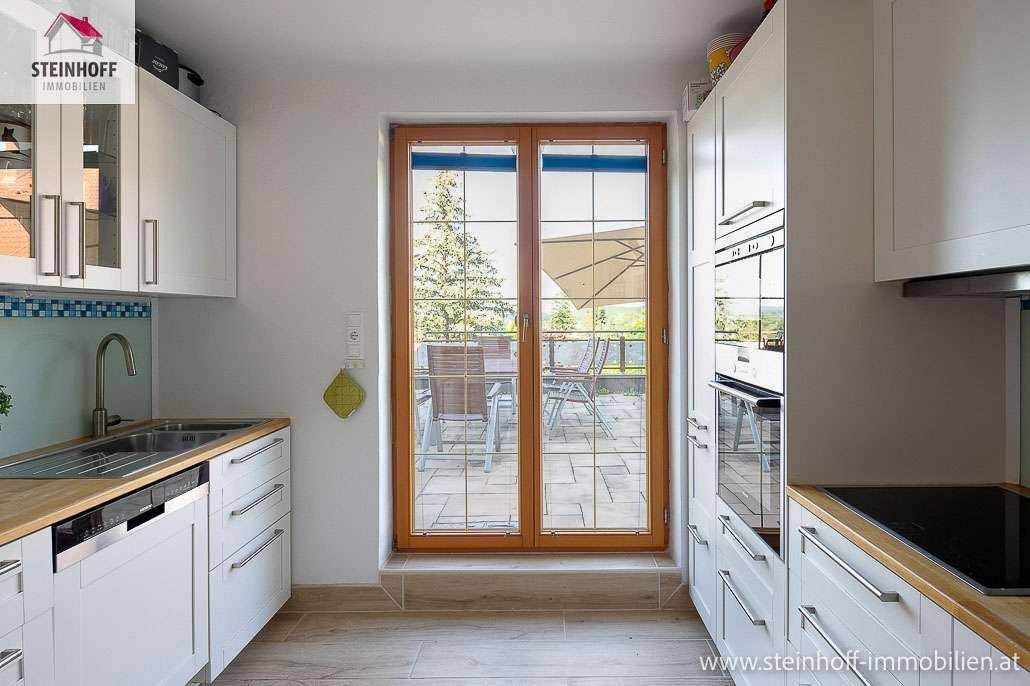 Funktionale Küche mit weißen Schränken, Holzarbeitsplatte und Blick auf die Terrasse.