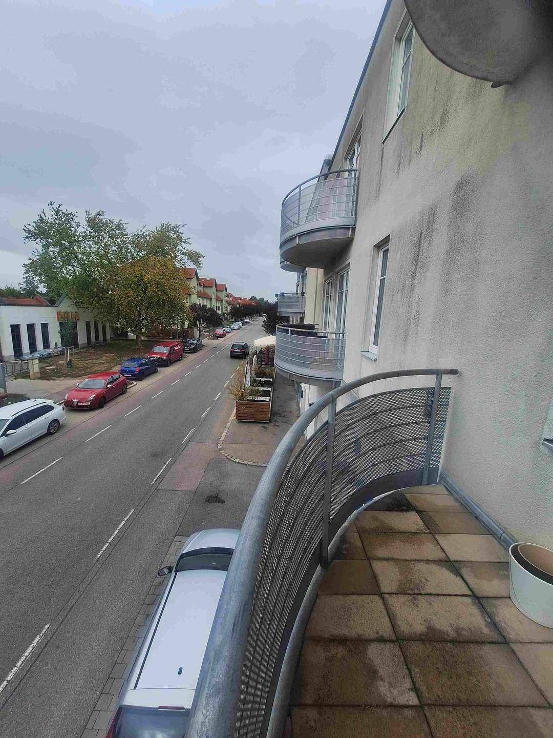 Seitlicher Blick vom Balkon entlang der Straße, zeigt weitere Balkone des Gebäudes und parkende Fahrzeuge.
