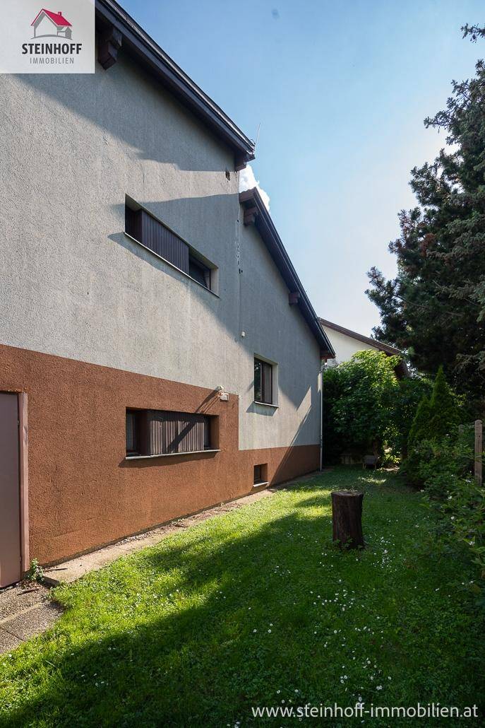 Seitenansicht des Hauses mit einer gepflegten Rasenfläche und hohen Bäumen im Garten.