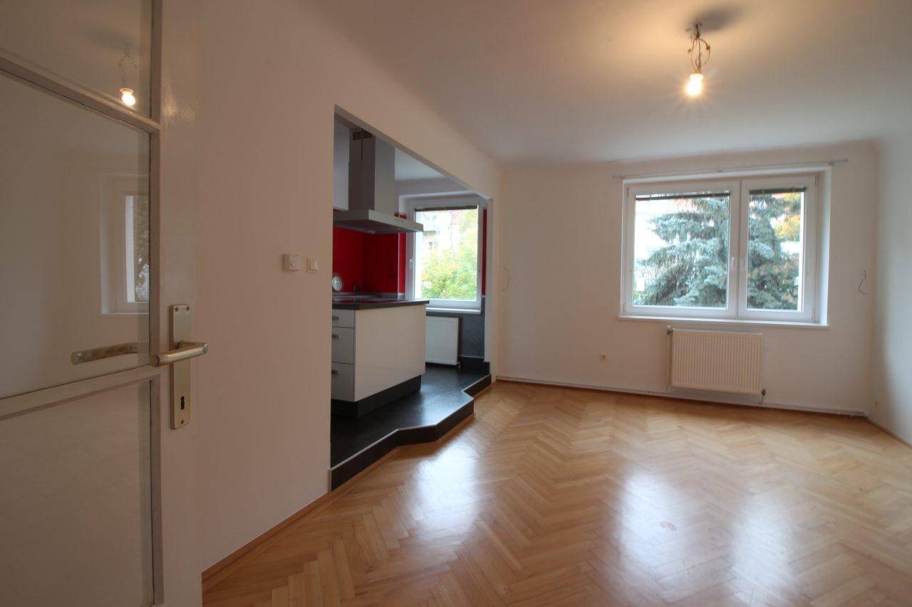 Geräumiger Wohnbereich mit Fischgrätparkett und Blick ins Grüne durch das Fenster.