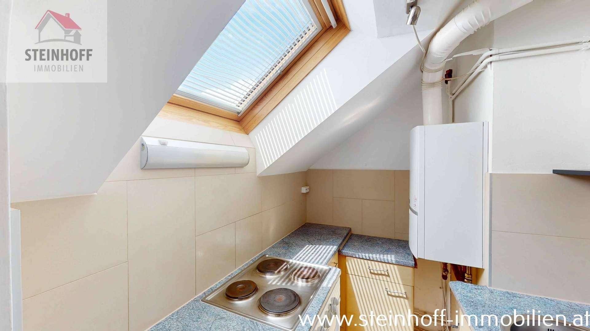 Kleine Küche mit Dachfenster, Kochfeld, Spüle und Dachschrägen.