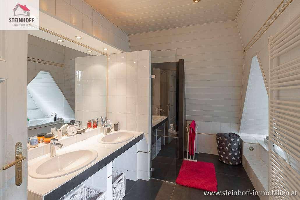 Helles Badezimmer mit Doppelwaschbecken, großem Spiegel und beheiztem Handtuchhalter.