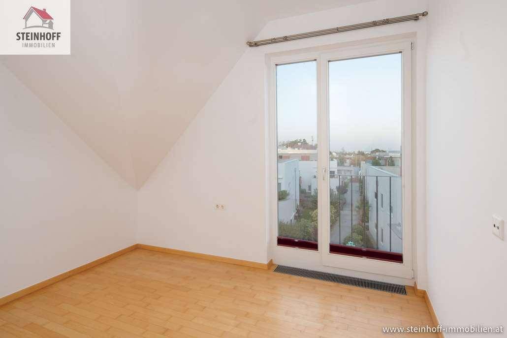 Heller Raum mit Holzboden und Fenster, das einen Blick auf die umliegenden Gebäude freigibt.