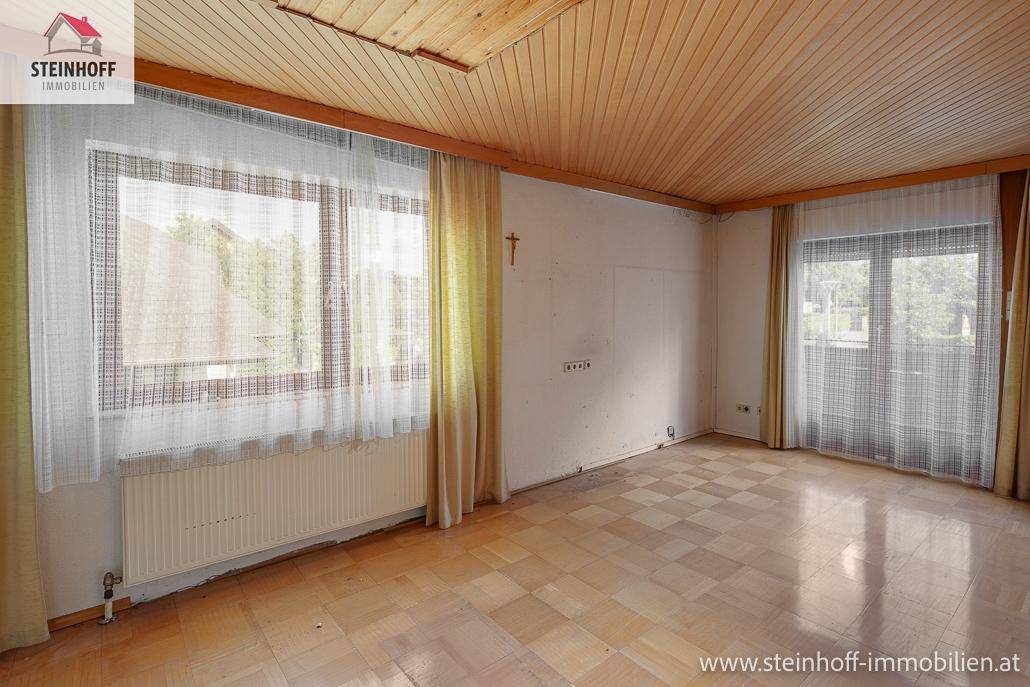 Geräumiger Raum mit Parkettboden, Holzdecke und großen Fenstern, die viel Tageslicht hereinlassen.