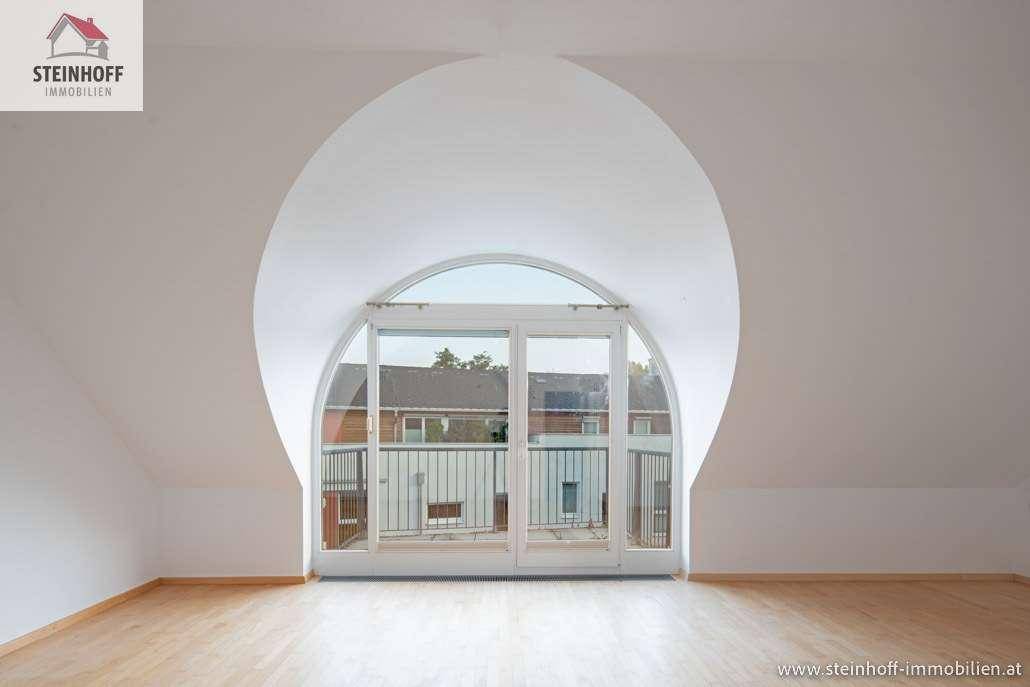 Heller Raum mit Holzboden und einem großen, bogenförmigen Fenster, das Zugang zum Balkon bietet.