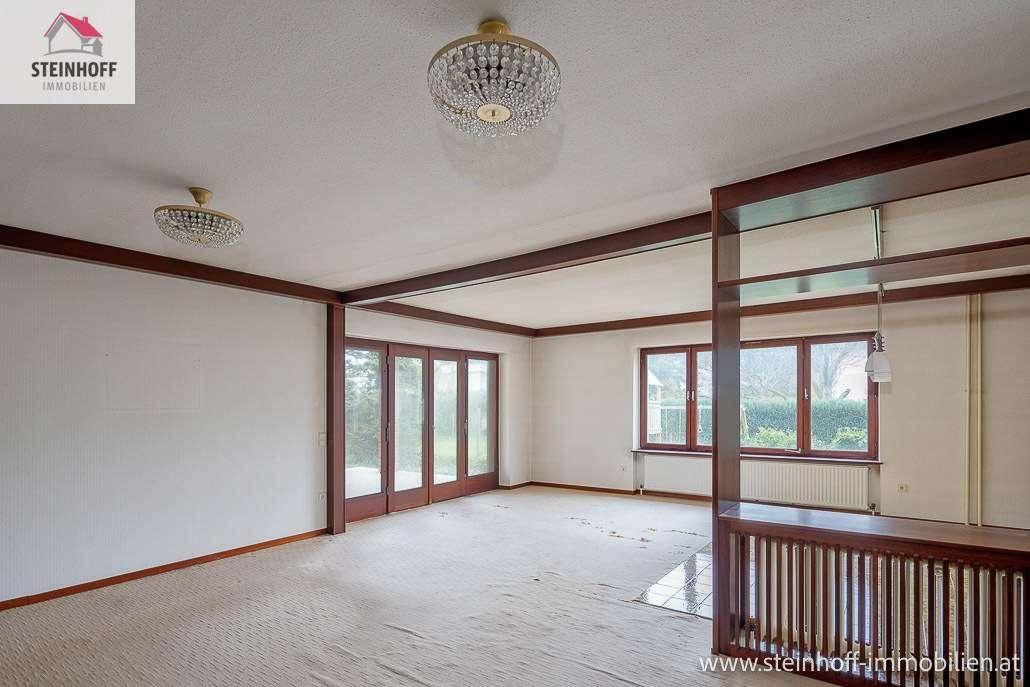 Geräumiges Wohnzimmer mit Teppichboden und großen Fenstern, die viel Licht hereinlassen.