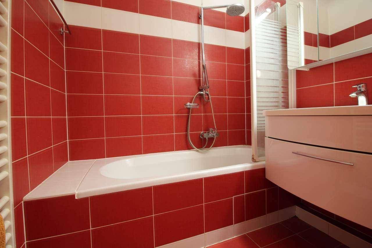 Helles Badezimmer mit rot-weißen Fliesen, Badewanne mit Duschvorrichtung und modernem Waschtisch.