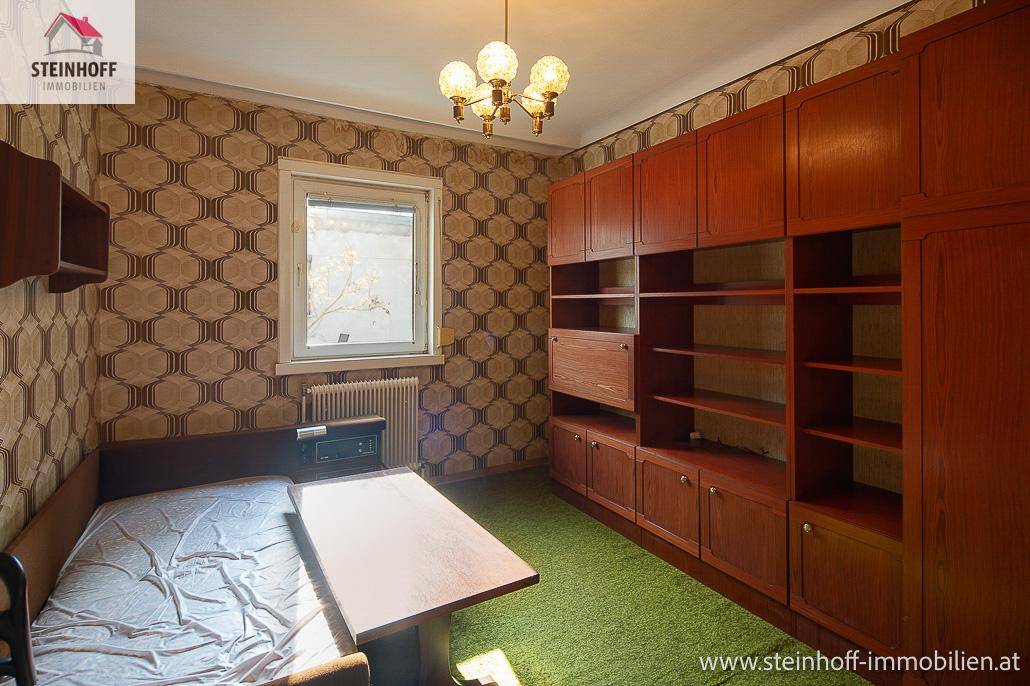 Zimmer mit Einzelbett, großer Schrankwand und gemusterter Tapete.