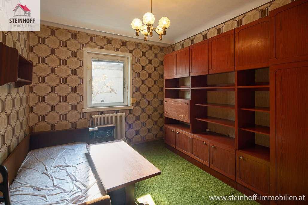 Zimmer mit Einzelbett, Holzschränken, gemusterter Tapete und grünem Teppichboden.