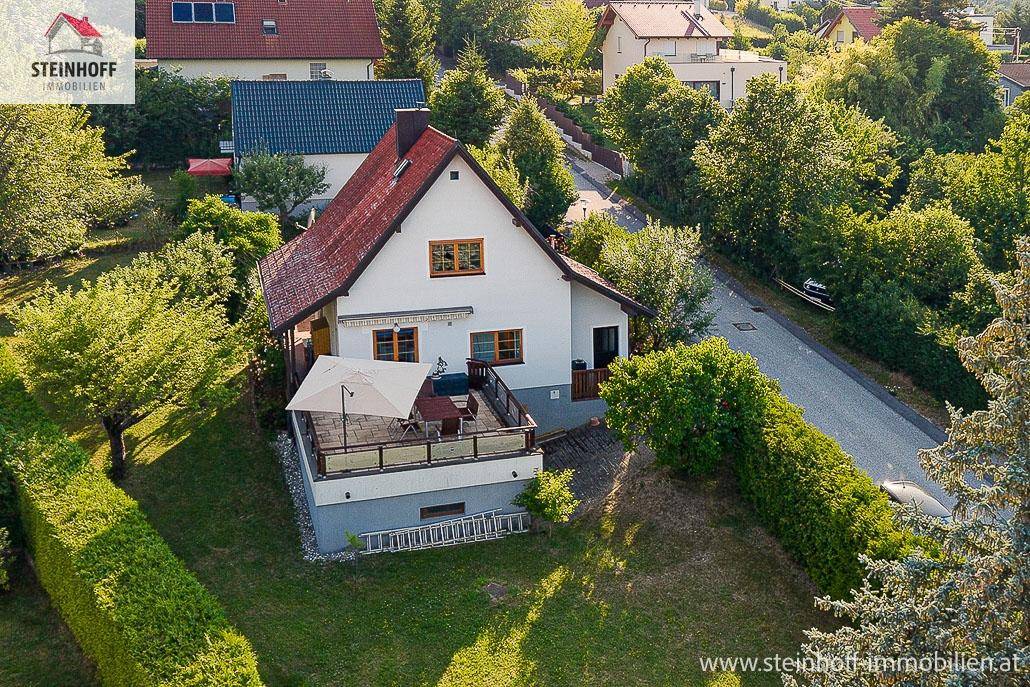 Haus mit großer Terrasse und Garten, eingebettet in eine grüne Landschaft.