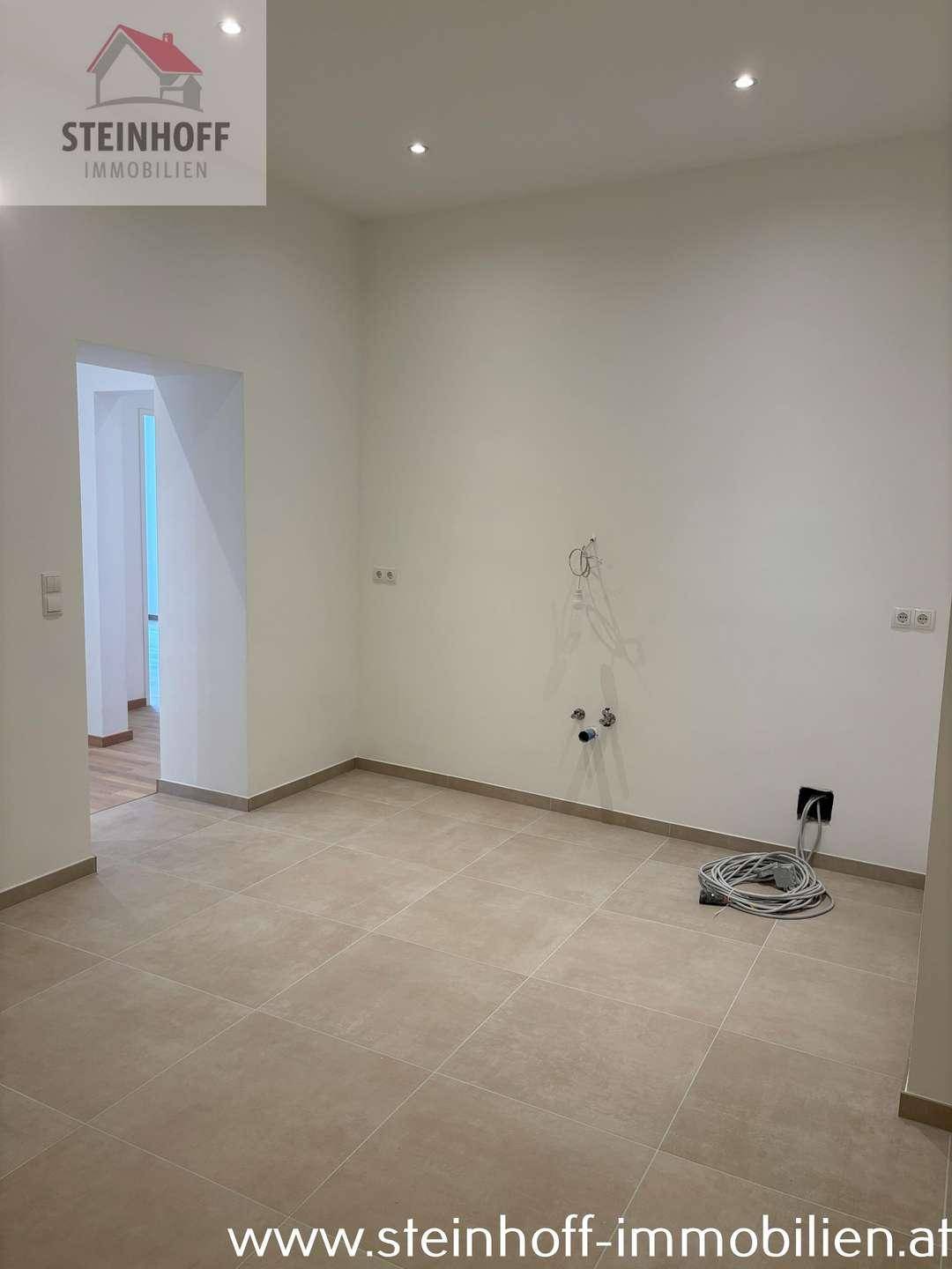 Geräumiger Küchenbereich mit Fliesenboden und vorbereiteten Anschlüssen für Küchengeräte.