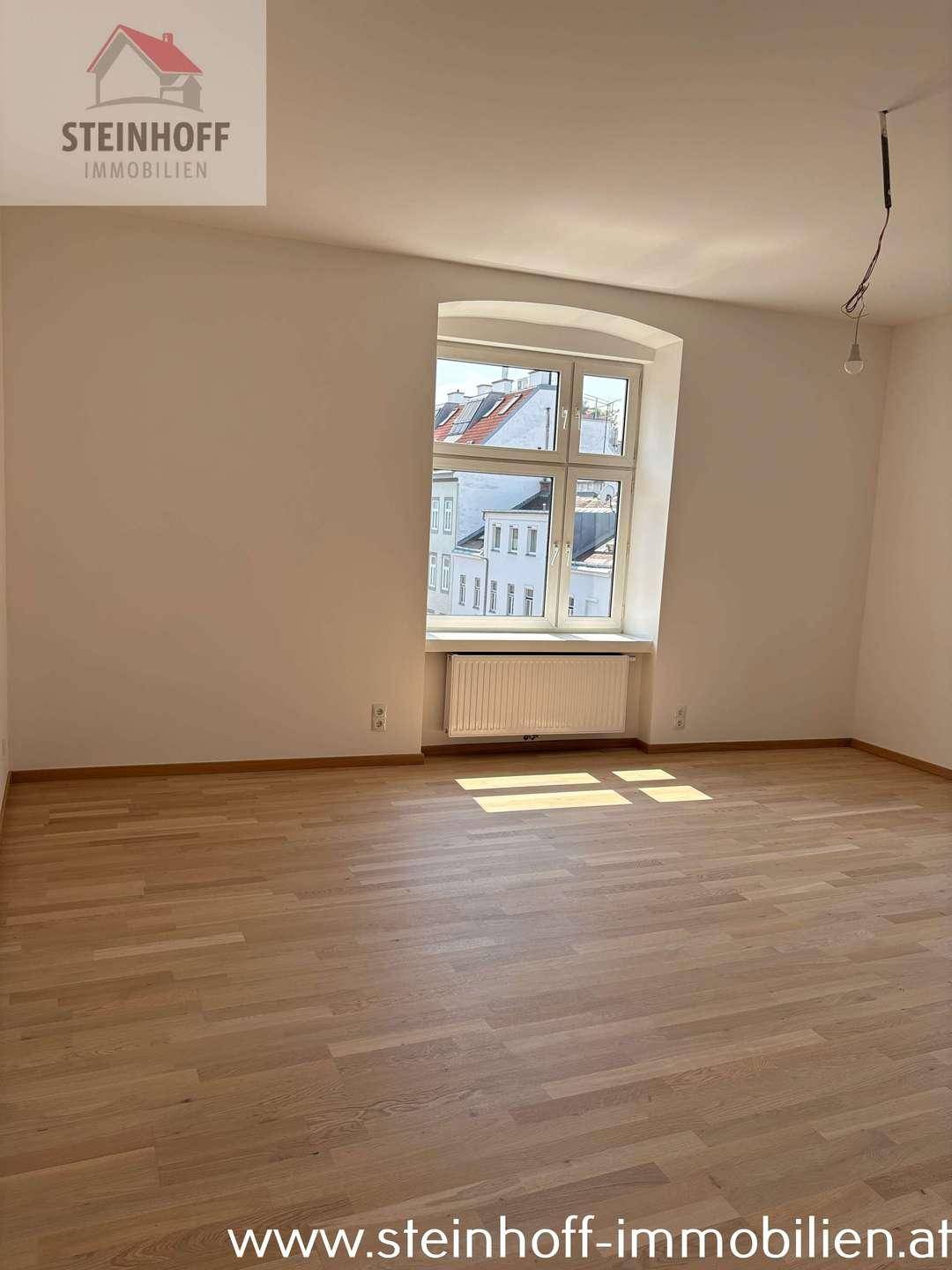 Geräumiges Zimmer mit hellem Parkettboden und einem großen Fenster, das den Raum erhellt.