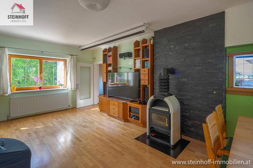 Wohnzimmer mit Kaminofen, Holzboden und Medienmöbeln an einer Schieferwand.