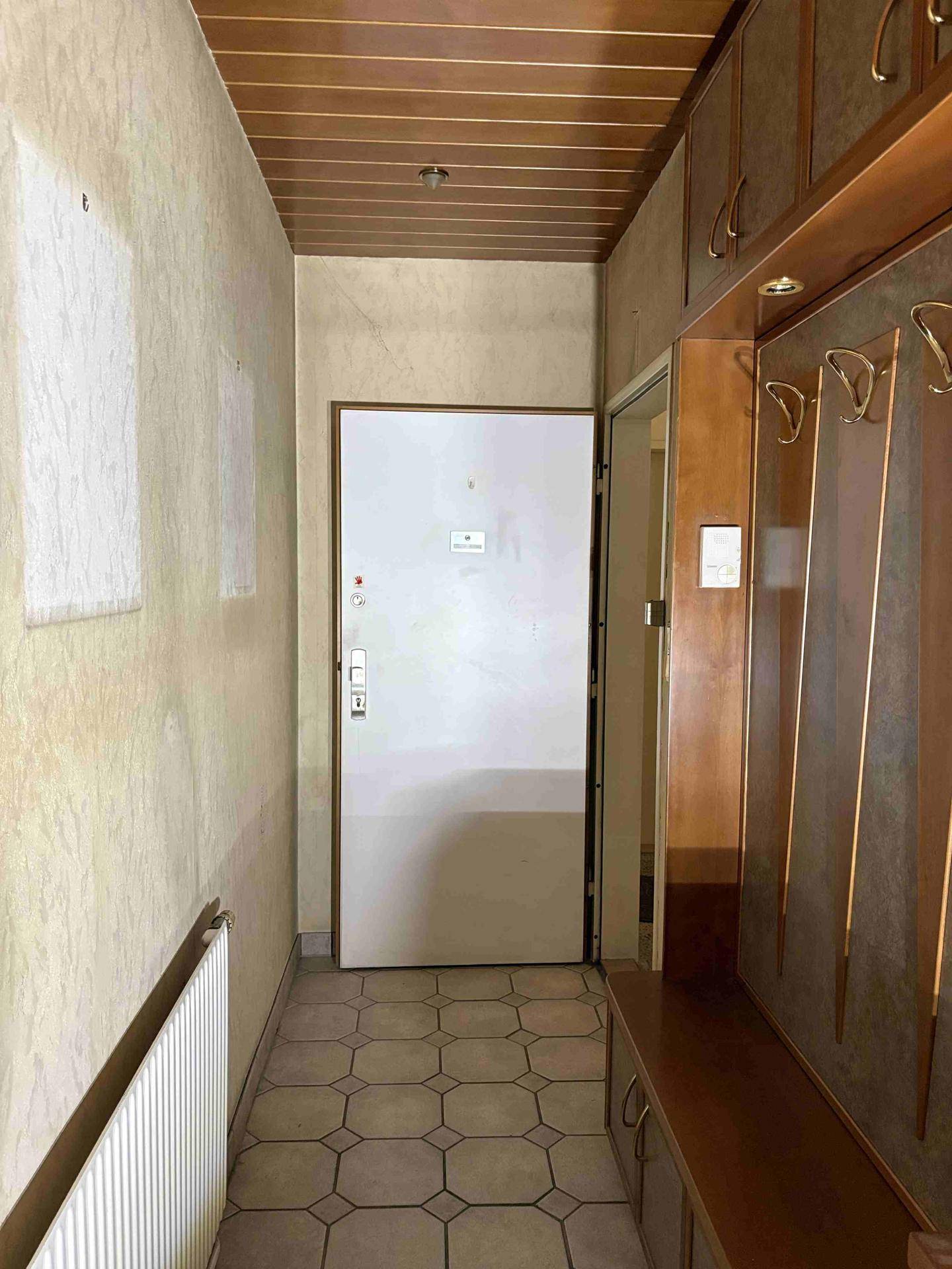 Eingangsbereich mit Fliesenboden, Holzdecke und Garderobe, der zur Wohnungstür führt.